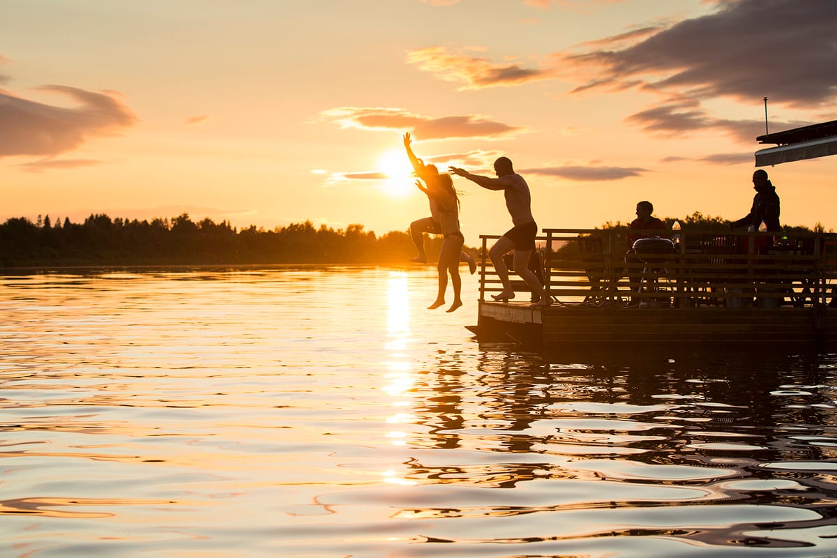 People jumping to swim from sauna raft Erkin Arkki during midnight sun in summer, in Rovaniemi, Lapland, Finland