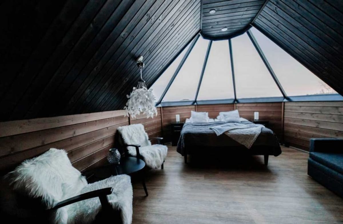 Wooden room with dark ceiling. Double bed and two chairs covered with sheepskin rug.